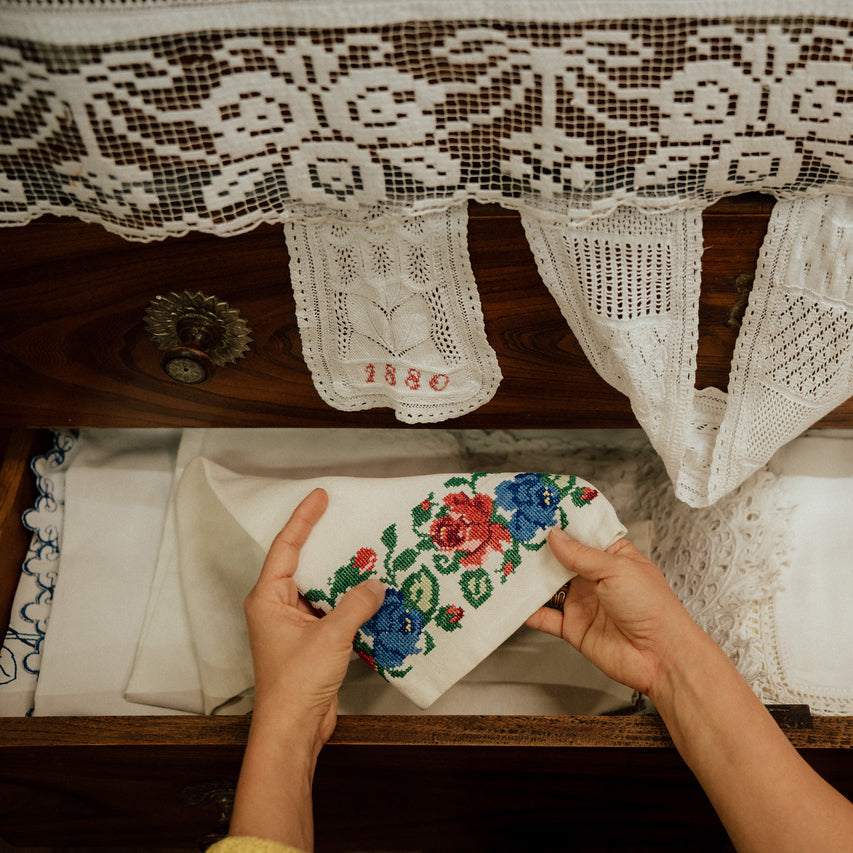 Hands holding vintage embroidered Moravian textiles in an old wooden drawer at Kobylí museum, showcasing traditional craftsmanship and family heritage.